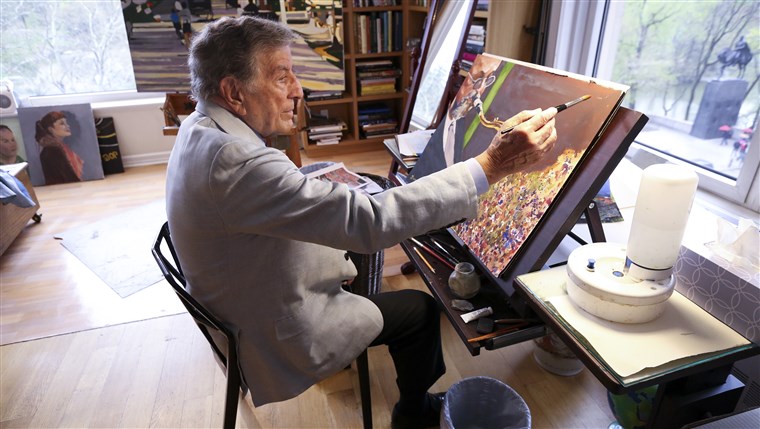 ב his New York art studio, Tony Bennett finishes a painting while sitting among several of his completed works. 