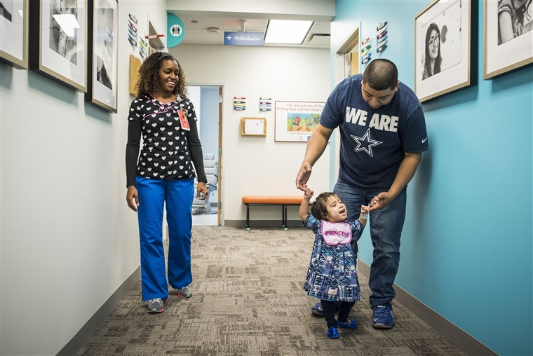 אריק Mata holds daughter Knatalye’s hands as she walks down the hall of a clinic at Texas Children’s Hospital.