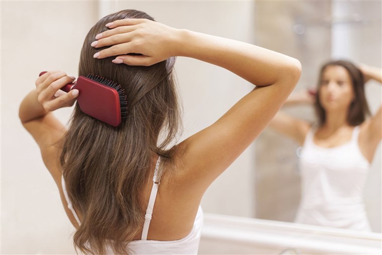 צעיר woman brushing healthy hair in front of a mirror