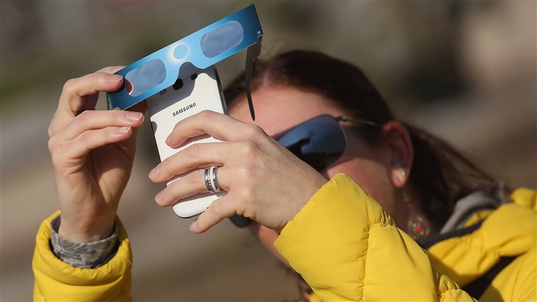  woman uses special glasses and a smartphone to photograph eclipse