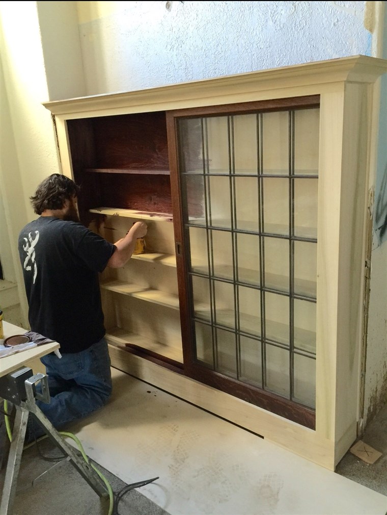 हारून Gray, one of the Singing Contractors, paints wood stain onto cabinets he built.