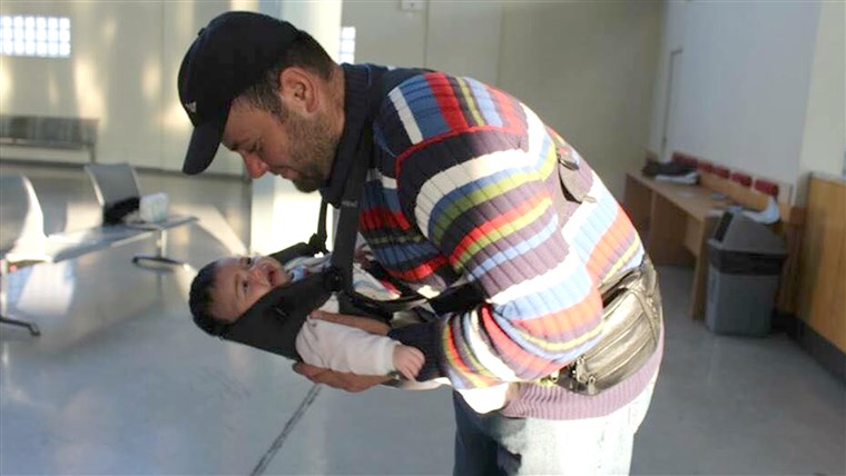  father adjusts his one-month-old daughter in a donated baby carrier. His baby was born in Lebanon, and he said the family was fleeing Syria because it was no longer safe to raise. Even though baby-wearing is not prevalent in Syrian culture, many of the men like to be in charge of carrying the baby, as they have been leading the family through dangerous situations.